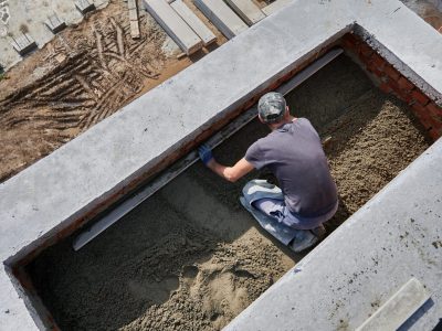 Top view of male contractor placing screed rail on the floor covered with sand-cement mix at construction site. Man worker leveling surface with straight edge while screeding floor in new building.